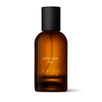 Amber glass Aesop Unforeseen Aer Eau de Parfum bottle with black cap on a white background.