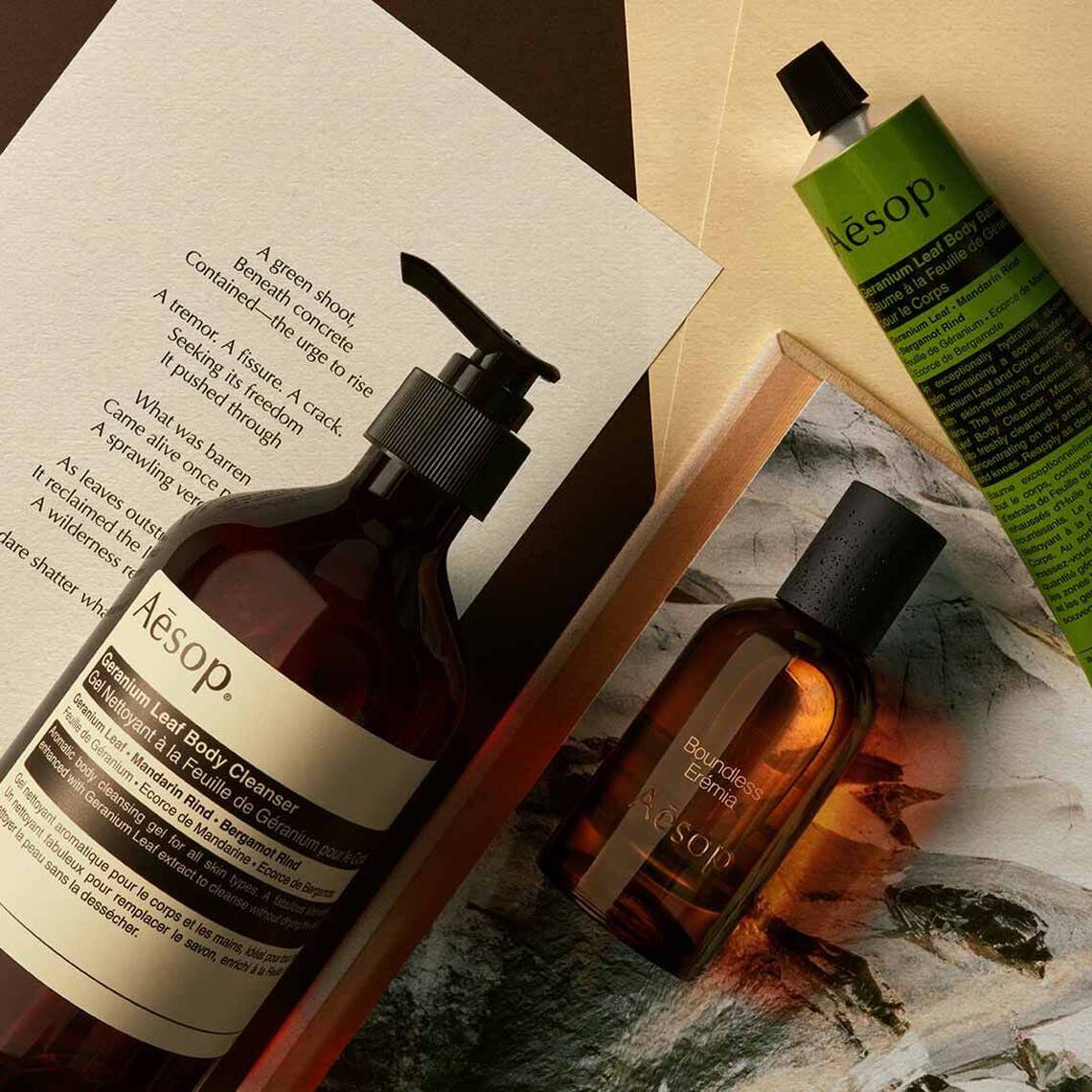 Aesop Boundless, Eremia fragrance bottle, large amber pump bottle and cosmetic tube on open books and printed pages.