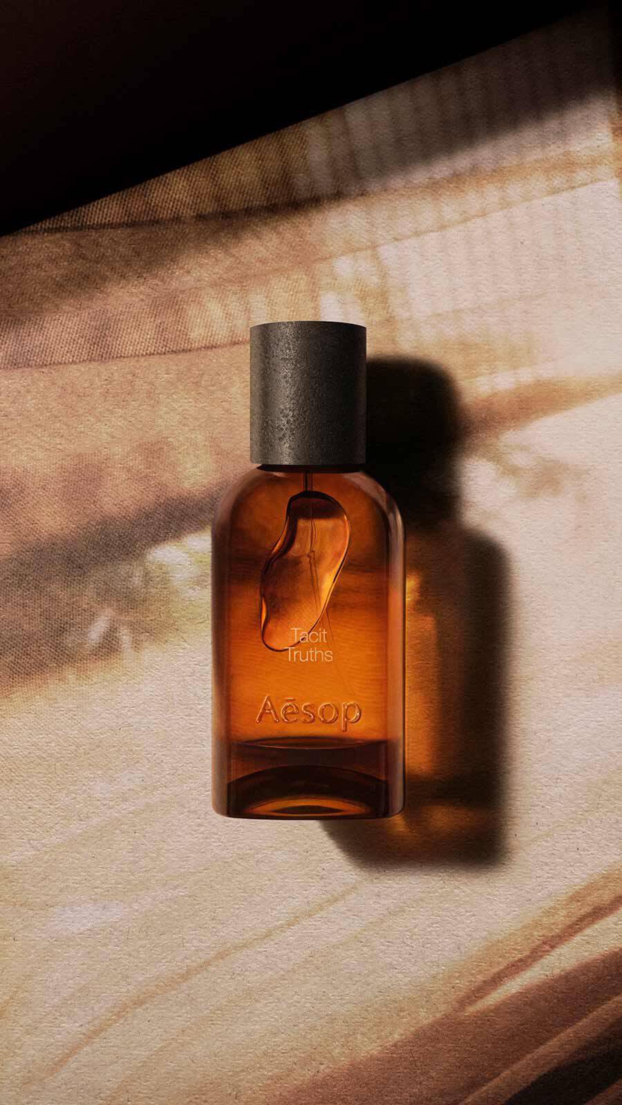 Aesop Tacit Truths Eau de Parfum bottle with black cap on a pale warm wooden surface with warm light and shadow stripes.