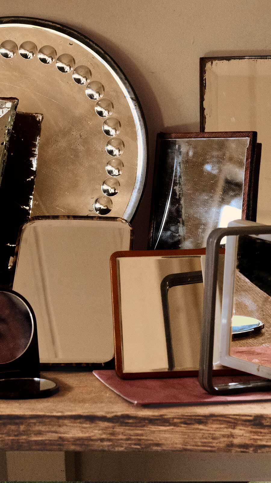 Collection of vintage mirrors and frames in dark wood and tarnished metal on a wooden dresser.