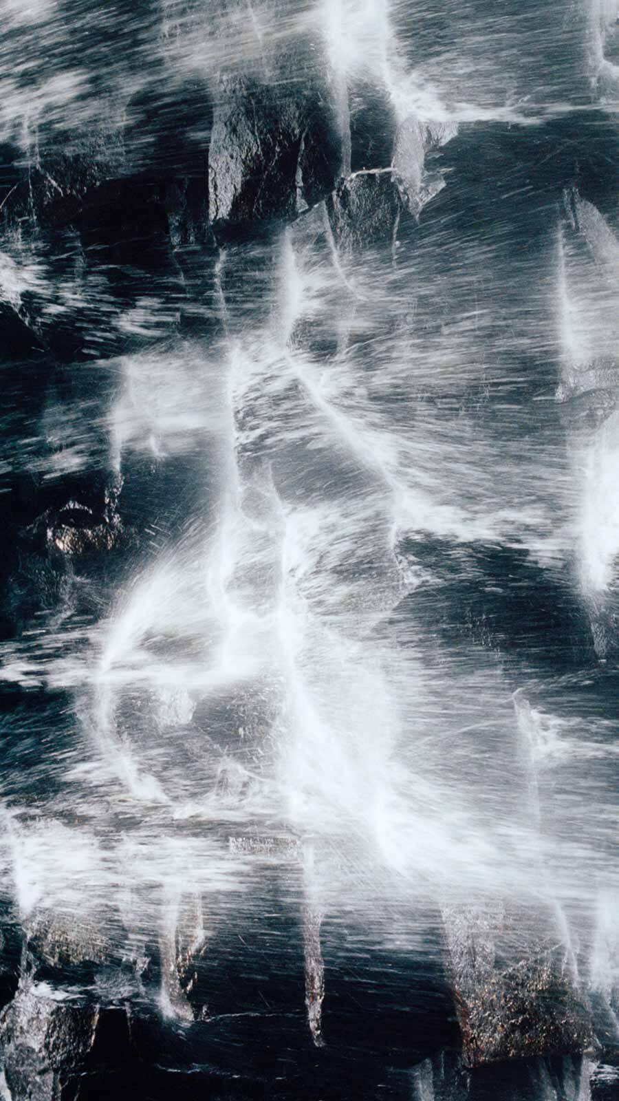 Close-up of rushing white water flowing over dark blue-grey rocks.