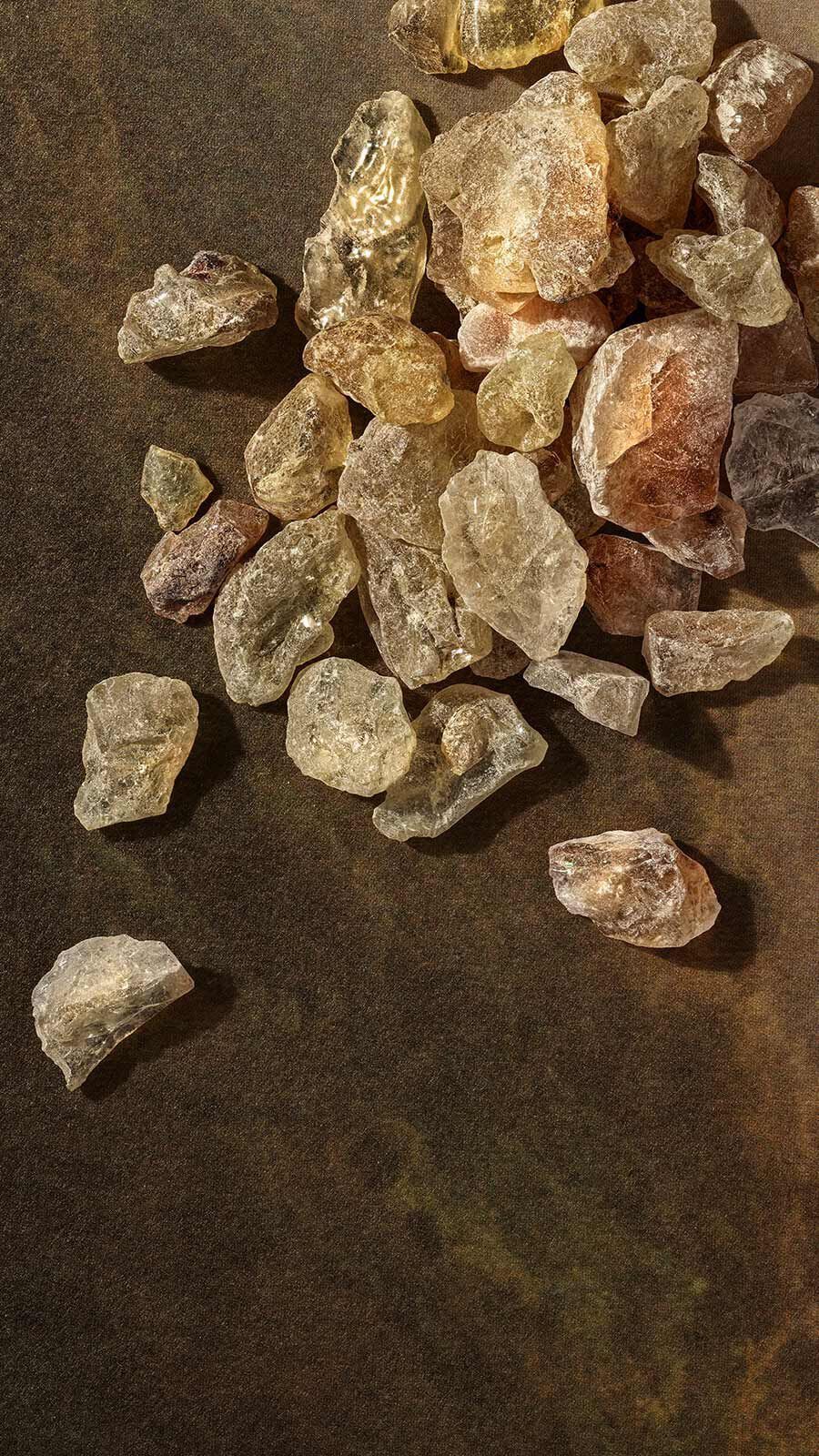 Pale golden frankincense resin crystals in a loose pile on a dark stone surface.