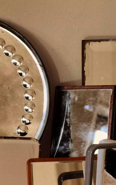 Stacked metallic and stone objects in bronze, beige and dark brown tones, arranged as overlapping geometric forms against a neutral wall.