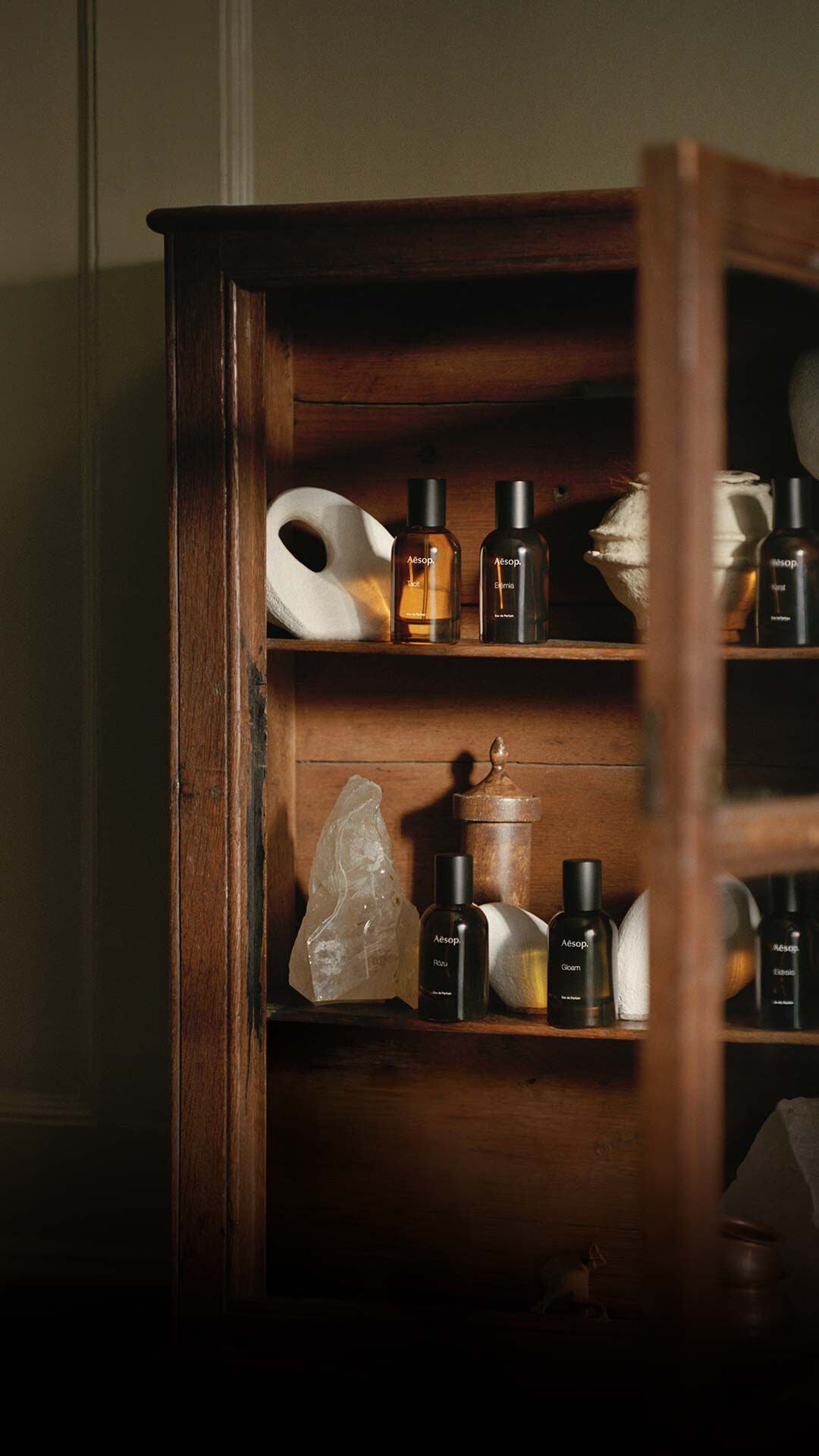 Open wooden cabinet filled with Aesop bottles in warm light.