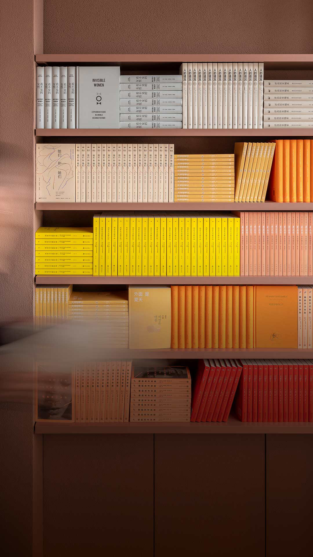 Small row of colourful books on a dark maroon shelf beside ribbed columns.