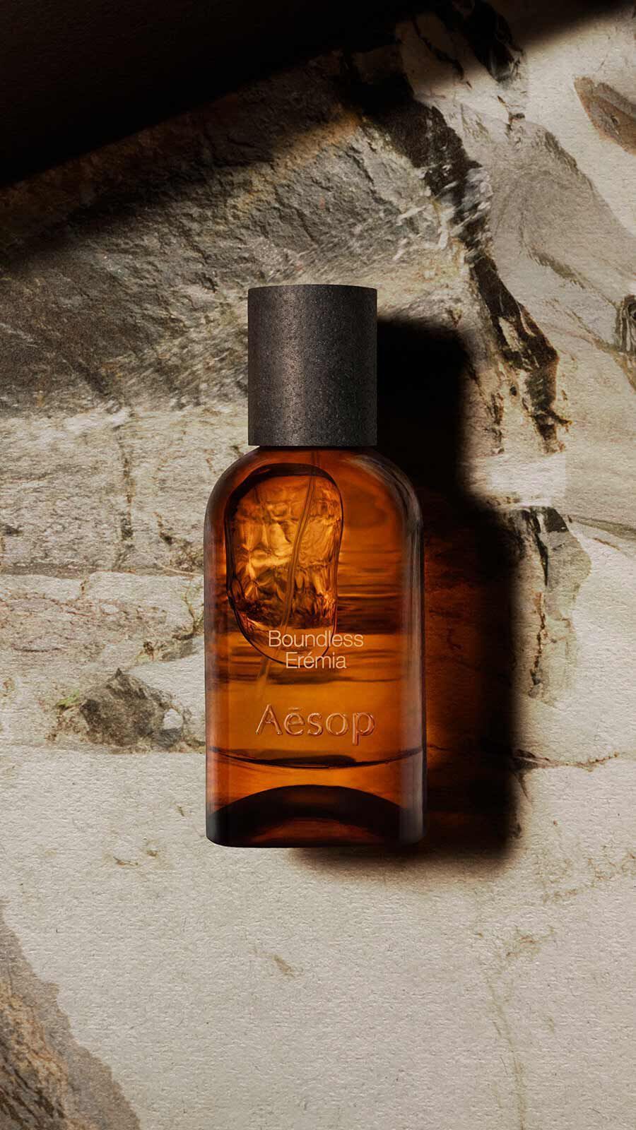 Aesop Boundless, Eremia Eau de Parfum bottle with black cap resting against a weathered pale stone wall in warm directional light.